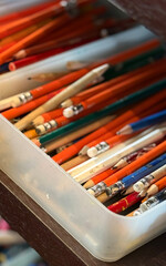 Naklejka premium Numerous colored pencils and graphite pencils in various shades of orange, blue, and green are organized within a transparent plastic tray. The pencils feature erasers and sharpened tips, suggesting