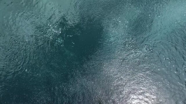 Top down abstract view of dark blue water surface with ripples, textured liquid movement, fluid dynamics and glittering light reflections