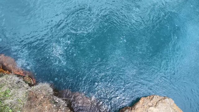 Top view of turquoise mineral water bubbling in a natural volcanic spring, rocky geothermal pool edge, volcanic nature background, geology research, hydrothermal activity, warm spring water