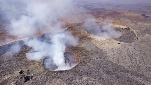 Aerial view of Erta Ale volcano with thick volcanic smoke rising from the crater, surrounded by rugged lava fields and barren desert landscape in Zone 2, Afar, Ethiopia.