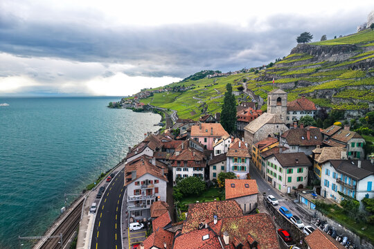 Aerial view of Saint-Saphorin village with historic stone buildings and terracotta rooftops nestled between terraced vineyards and Lake Geneva in Saint-Saphorin, Vaud, Switzerland.