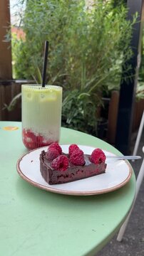 Chocolate tart topped with fresh raspberries served with an iced matcha latte in a garden caf&eacute;. Dessert and refreshing drink on an outdoor table in natural daylight.