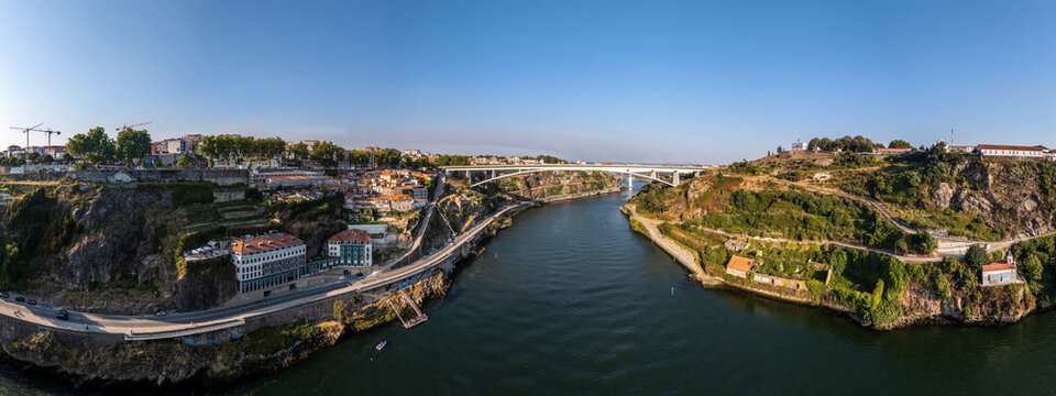 Aerial view of the Ponte Infante Dom Henrique bridge spanning the Douro River, connecting the historic urban landscape with lush green hillsides in Vila Nova de Gaia, Porto, Portugal.