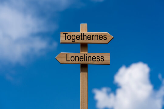 Wooden signpost with togetherness and loneliness words.. Wooden directional sign post with words Togetherness and Loneliness pointing in opposite directions under blue sky with clouds