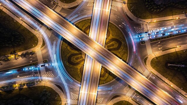 Perfect Vertical Aerial Night View of Modern Circular Highway Interchange with Long Exposure Traffic Light Trails and Symmetrical Urban Infrastructure