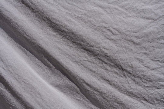 Top view macro texture of crumpled grey fabric. Full frame closeup background of soft crumpled grey or lavender textile material with natural folds creases and soft diagonal shadows