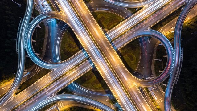 Perfect Vertical Aerial Night View of Modern Circular Highway Interchange with Long Exposure Traffic Light Trails and Symmetrical Urban Infrastructure