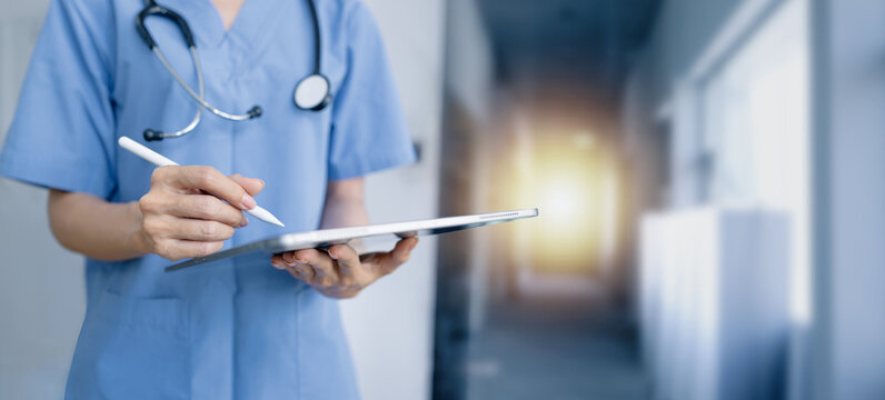 female nurse or doctor and a stethoscope, holding and using a digital tablet inside a hospital or clinic.	

