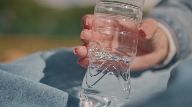 Caucasian woman gripping chilled water bottle, street photographer taking sunlit hydration break on denim blanket, condensation beads and sparkling droplets, closeup on fingers and palm, lively