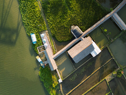 Aerial view of a building with a long rooftop walkway along the Serayu River, surrounded by lush green fields and water in Kecamatan Rawalo, Jawa Tengah, Indonesia.