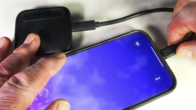 Closeup of a man&rsquo;s hands connecting a portable SSD, external hard drive, to a mobile phone, with a short USB cord or cable, for extra file storage capacity.