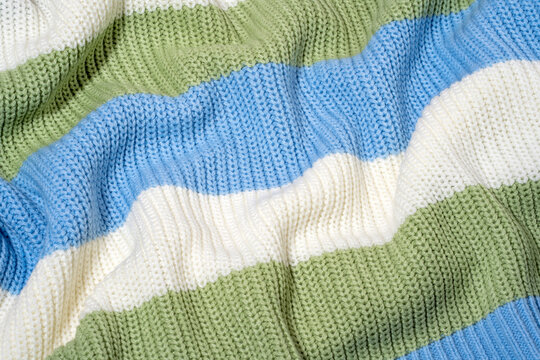 Close-up of blue, white and pastel green color striped sweater texture in soft folded knitwear. Concept of tactile textile detail, wardrobe choice for cold winter and autumn season