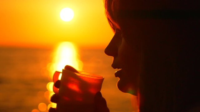 Oceanfront beverage moment captures a silhouette of a woman sipping tea at sunset. Static close-up shot.
