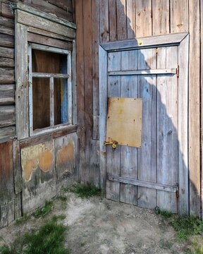  An old weathered wooden house corner with a vintage window and a door patched with plywood
