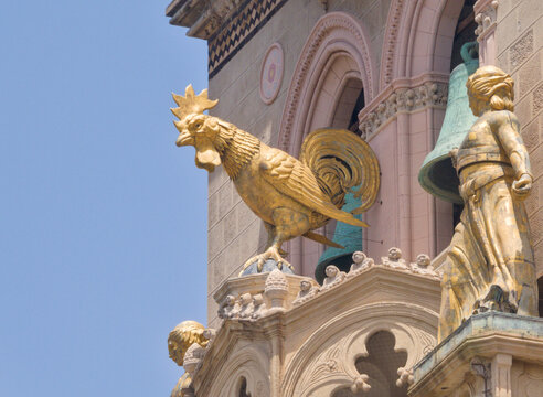 Gilded mechanical golden rooster statue and bronze bell ringers on the famous astronomical clock tower of Messina Cathedral in Sicily, Italy against bright blue summer sky.