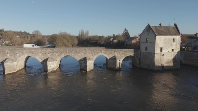 An aerial view crosses a long stone arched bridge spanning the Loire River beside a small riverside town.