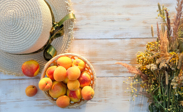 summer straw hat, fresh ripe harvested fruits - peaches, nectarines and field flowers on white rustic wooden table close up. copy space. flat lay