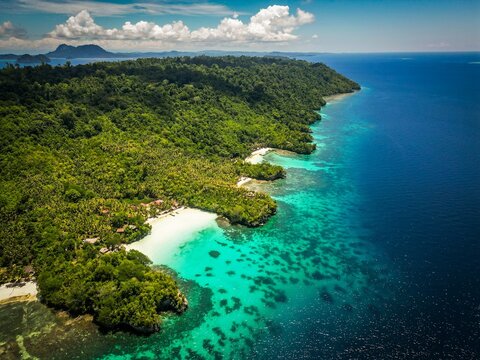 Aerial view of Togean island with lush rainforest, white sand beaches, and turquoise coral reefs surrounded by deep blue ocean in Tojo Una-Una Regency, Tojo Una-Una Regency, Indonesia.