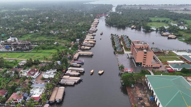 Drone view of houseboats lined along a backwater canal with a red bridge in the distance on the route to Pathiramanal Island, Kerala.