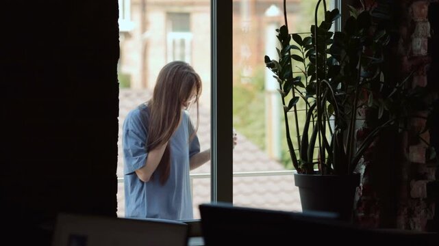 Young woman talking on smartphone during remote work day by window at home. Concept of remote work communication, flexible employment services, home office connectivity and team collaboration.