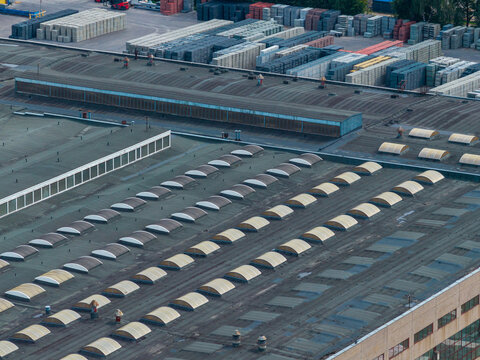 Aerial view of an industrial factory roof featuring numerous arched skylights and a large storage area with stacked pallets in the background in Vilnius, Vilnius County, Lithuania.
