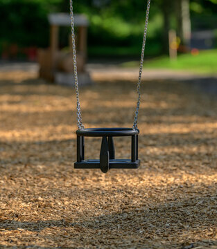 Empty toddler swing in quiet shaded playground suggesting childhood memory.