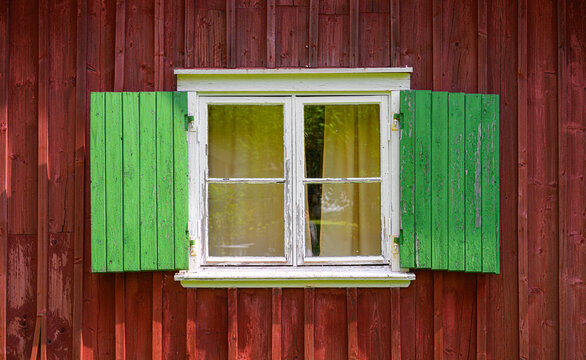 Old window with green shutters on red wooden wall.