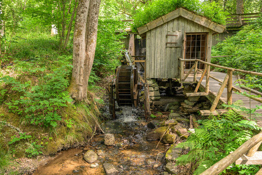 Historic wooden watermill with flowing stream in lush forest.