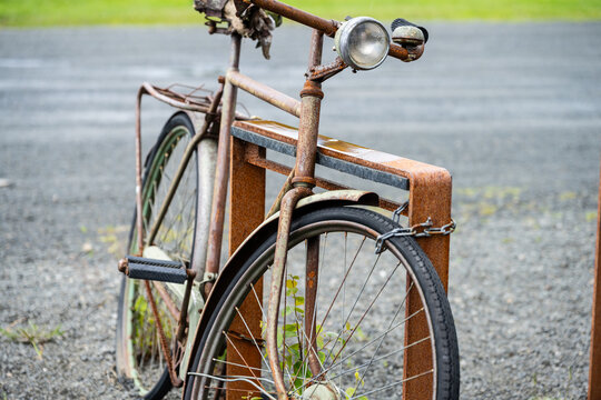 Rusty vintage bicycle locked to metal rack outdoors.
