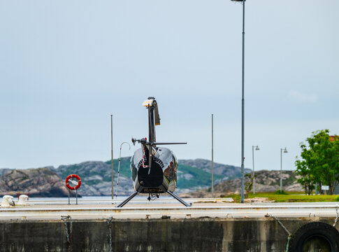 Small helicopter parked on coastal landing area facing open seascape.