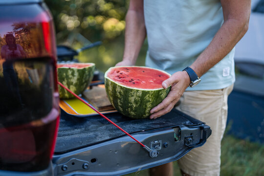 Man holding refreshing watermelon on truck tailgate during summer camping