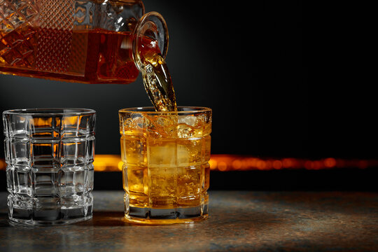 Whiskey is poured from a decanter into a glass with ice.
