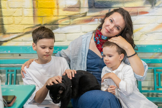 A Caucasian woman with her two sons and a cat in a cafe. Pet-friendly outdoor cafe.