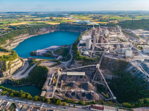 Aerial view of CCB Granulats Gaurain industrial quarry and cement plant with turquoise water basins, processing facilities, conveyor belts, and gravel stockpiles in Tournai, Wallonia, Belgium.