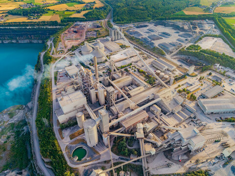 Aerial view of CCB Granulats Gaurain cement plant featuring large silos, conveyor systems, and a turquoise quarry lake surrounded by lush greenery in Tournai, Wallonia, Belgium.