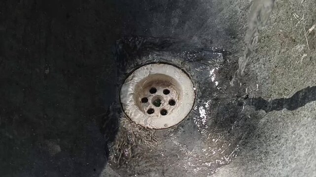 Close-up of clear water pouring into a stone basin drain hole. Flowing freshwater with natural stone texture and circular drain detail. IClean water, sanitation, conservation, and hygiene concept