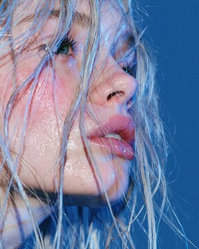 Extreme close up portrait of woman with wet platinum hair glowing skin and blue studio light Expression of luminous beauty