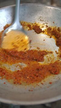 Cooking Thai stir fried fresh catfish in red curry paste. Sauteing red curry paste in oil, adding raw catfish slices, simmering with water, tossing Thai eggplants, red chili, and fresh holy basil in w