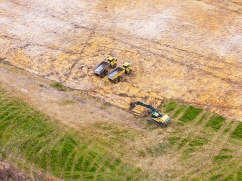 Aerial view of an excavator and two dump trucks working on a construction site in Valgunde Parish, Jelgava Municipality, Latvia.