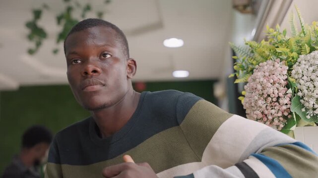 Black man making eye contact with gentle expression, floral bouquet nearby and soft ambient light, intimate closeup conveying sincerity, vulnerability and romantic connection during quiet cafe date