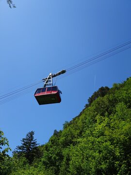 Meiringen, Switzerland, May 23, 2026. Red aerial cable car of the Luftseilbahn Hasliberg ascending over green forest.
