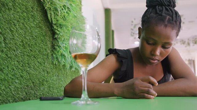 Black artist reading message on phone at green cafe table, calm acceptance replacing earlier sadness, fingers resting on tabletop near wine glass, introspective energy, subtle empowerment and quiet