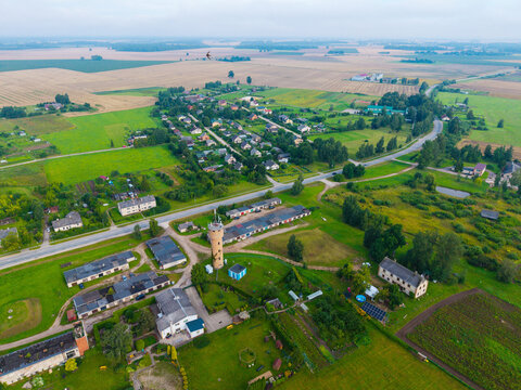 Aerial view of a water tower standing in the rural village surrounded by green fields, residential houses, and trees in Jaunberze, Dobele Municipality, Latvia.