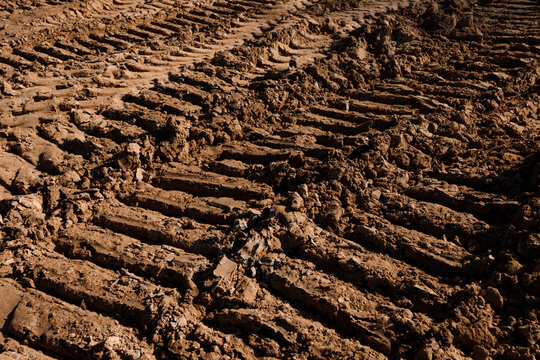 Heavy industrial tire tracks and crawler protector tread marks on wet muddy soil earth background at construction site field countryside dirt road agriculture landscape texture nobody closeup