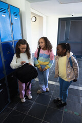 Obraz premium African American teenage girls standing by blue lockers in school corridor, opening black backpack