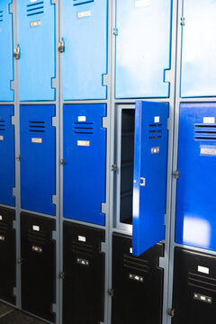 Middle-row blue locker door is standing ajar in metal locker bank, revealing empty shelves, padlock