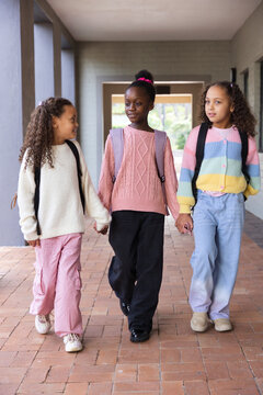 African American teenage girls walking in school corridor, holding backpacks and sweaters