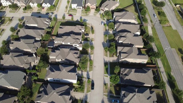 Orderly suburban houses with multi gable roofs align along quiet street in DFW metroplex. Birds eye view reveals geometric shingle patterns, attached garages, paved driveways, yards, Frisco, TX