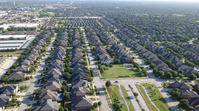 Green neighborhood lawn with stone pavilion sits among housing rows suburbs Dallas Fort Worth metroplex. High perspective two story homes, multi gable roofs, tree lined cul-de-sacs, Frisco, Texas