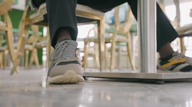 Cafe undertable sneaker closeup shows black woman college student nervously tapping foot under table during first date, wooden chairs, warm morning light, casual sneakers, subtle romance